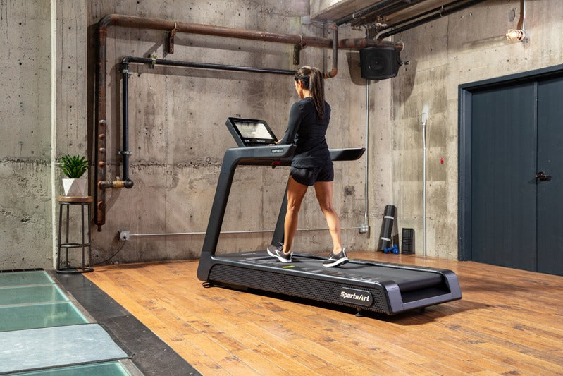 A woman using a treadmill in a modern indoor setting with concrete walls and wooden floor.