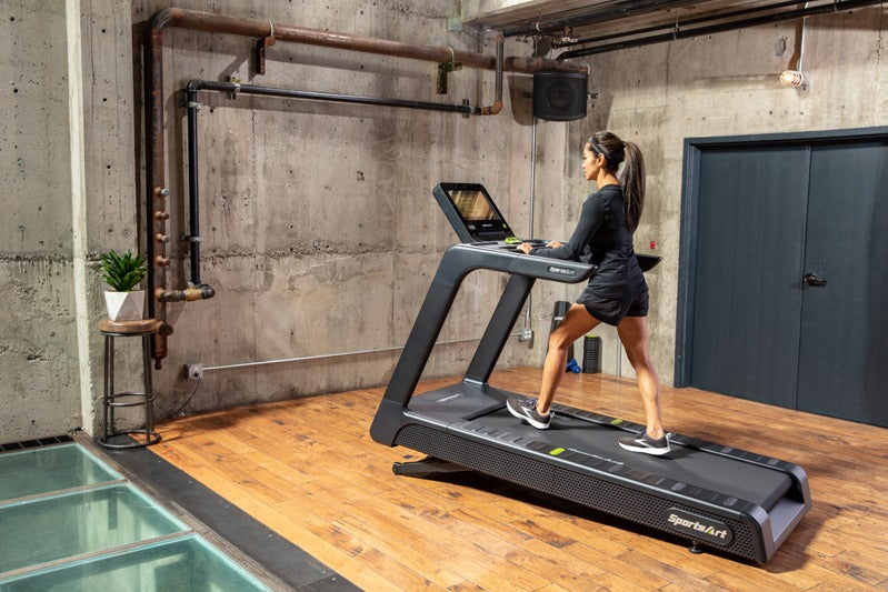 A woman using a treadmill in a modern indoor setting with concrete walls and wooden floor.