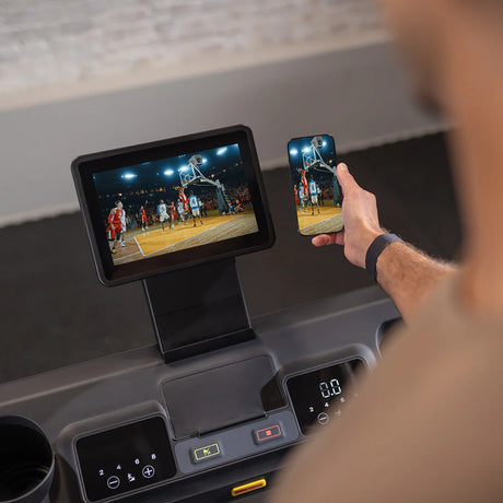 Person using a smartphone and tablet to watch a basketball game in a treadmill.