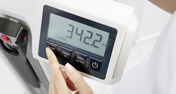 Digital weight scale with a hand pressing a button.