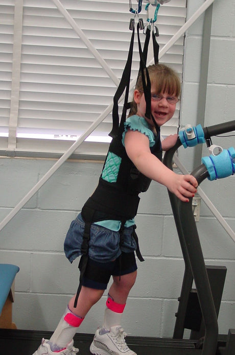 Child using a treadmill with safety harness and straps in a clinical setting